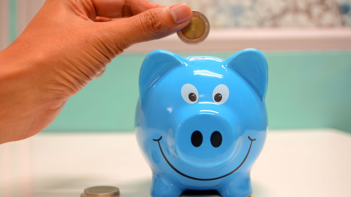 Hand dropping a coin into a piggy bank, illustrating regular Cash ISA saving